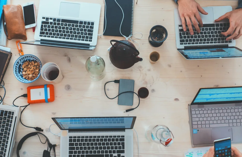 Overhead shot of multiple people working on various pieces of technology including laptops, phones and tablets