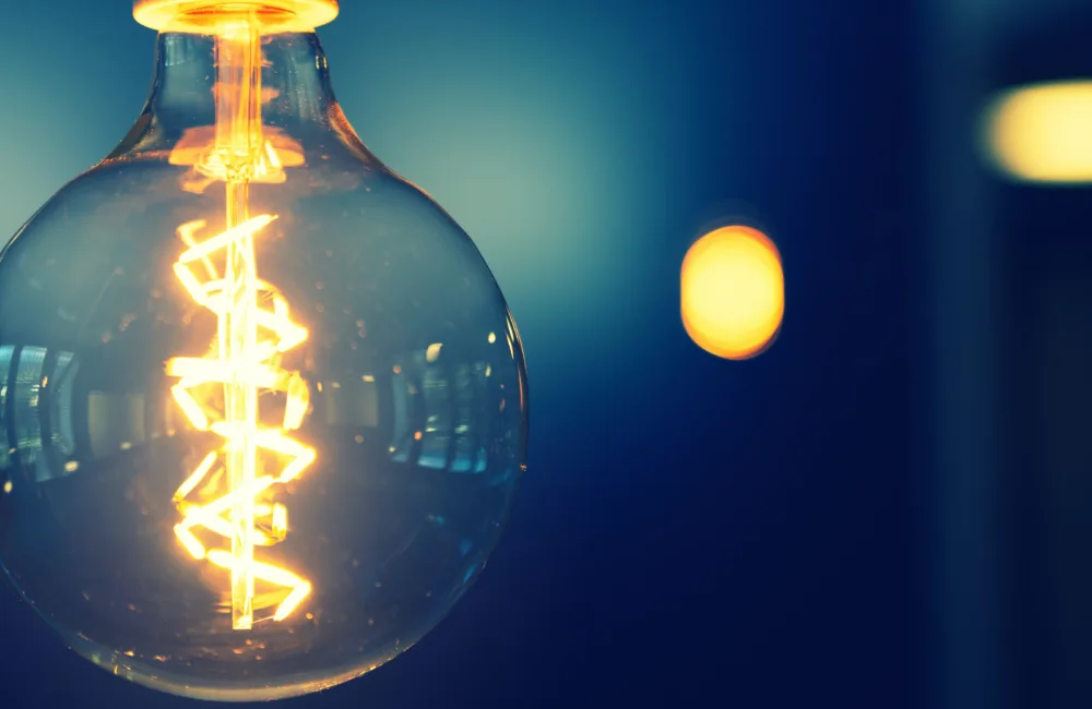 A circular light bulb with a glowing filament in front of a blue wall