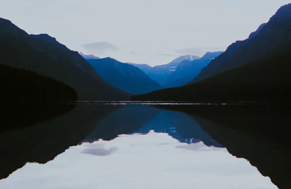 Silhouettes in blue and black of mountains reflected in a still lake