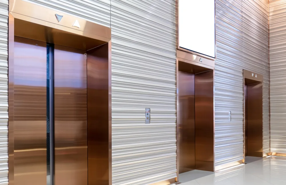 three brass lift door in reception area with gray cladded walls