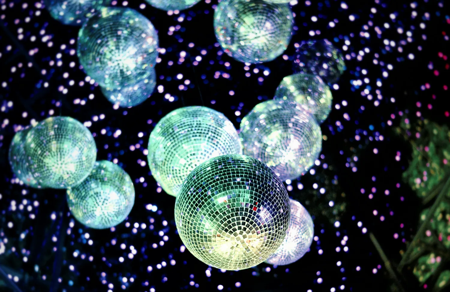 Disco balls hanging from a dark ceiling with colourful spotlights