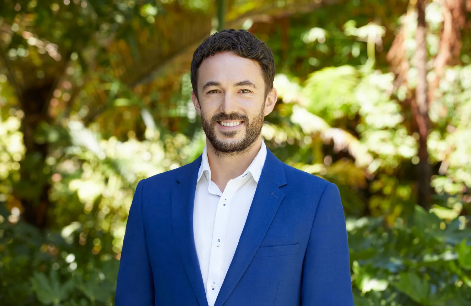 Oliver Grimaldi smiling towards the camera, standing outside in a white shirt and blue blazer