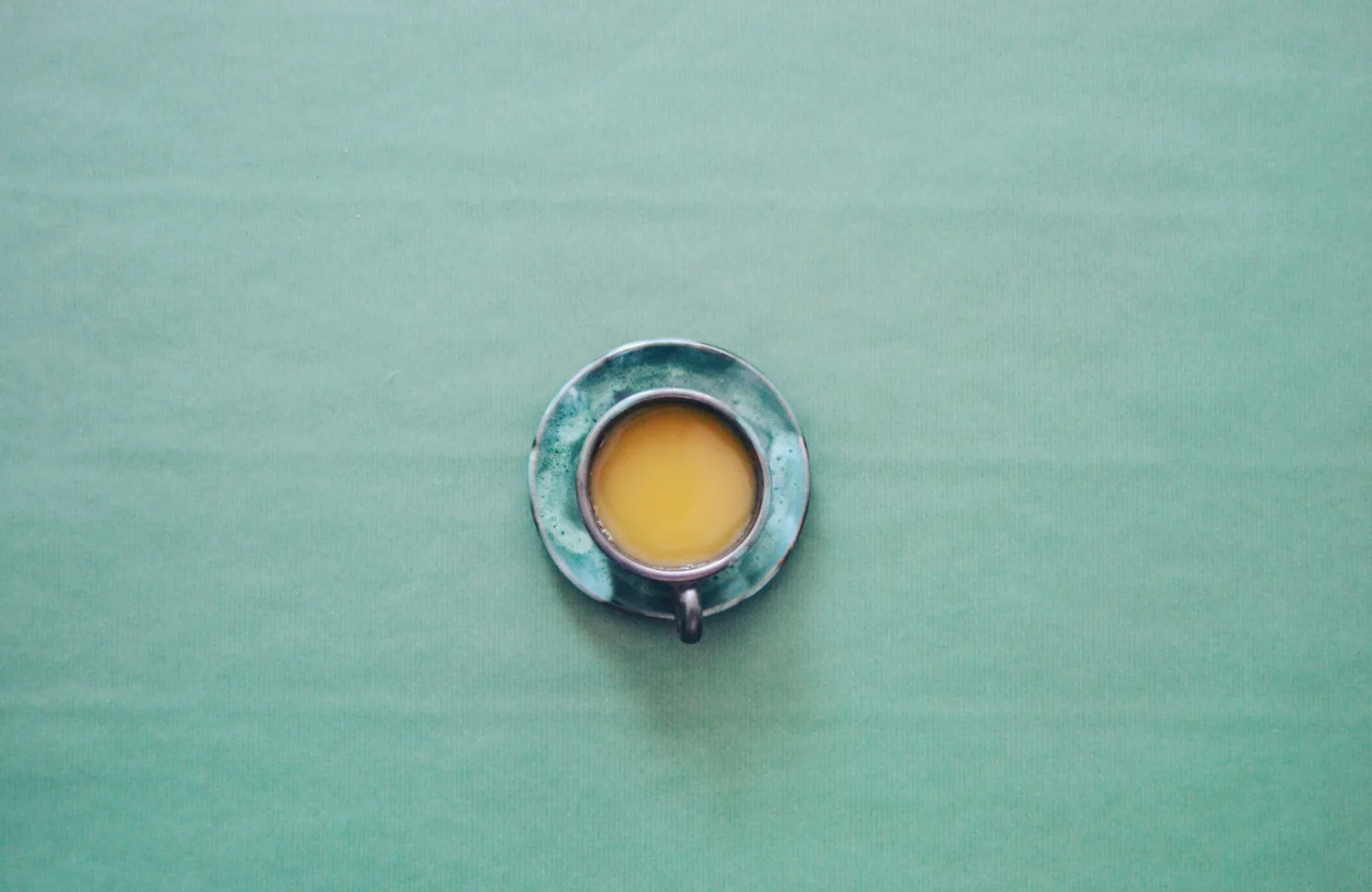Birdseye view of green cup and saucer with tea in sitting on a green tablecloth