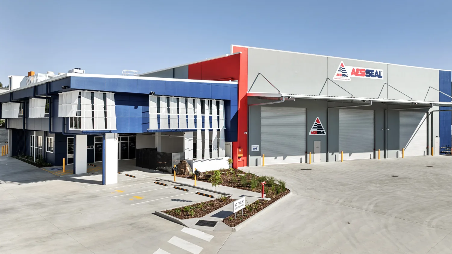Industrial building with blue office section and grey warehouse showing AESSEAL logo and three roller doors.