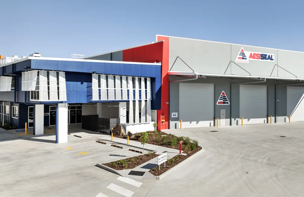 Industrial building with blue office section and grey warehouse showing AESSEAL logo and three roller doors.