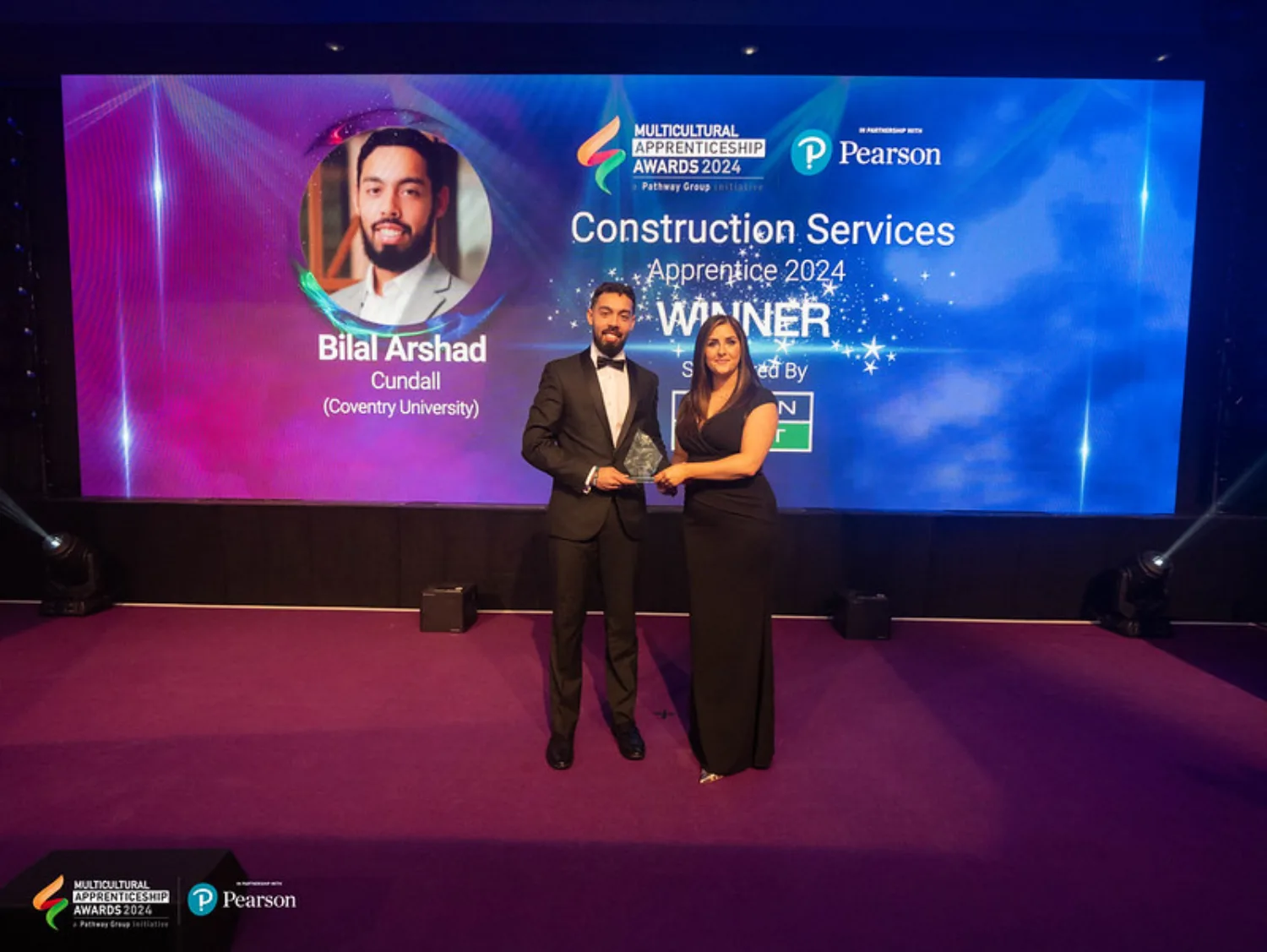 Bilal on stage collecting his award in front of a large Winner screen
