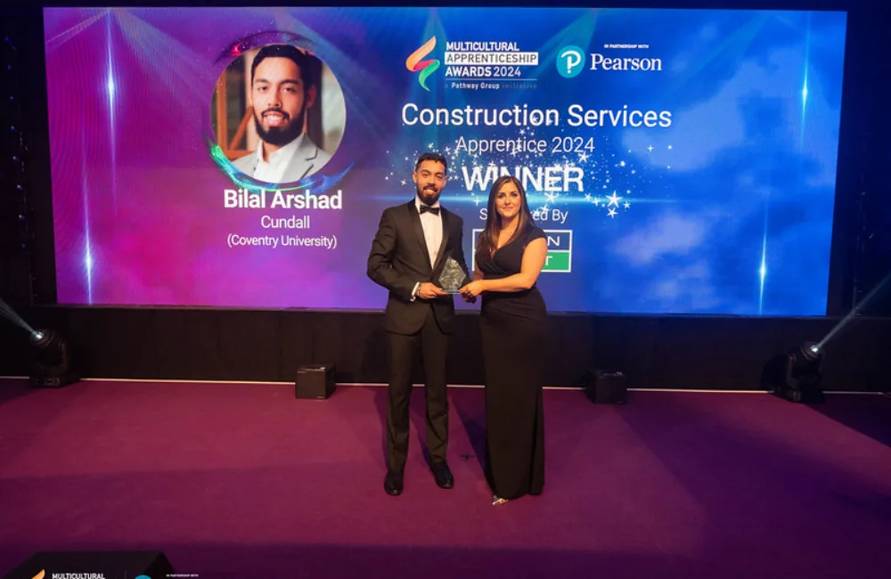 Bilal on stage collecting his award in front of a large Winner screen