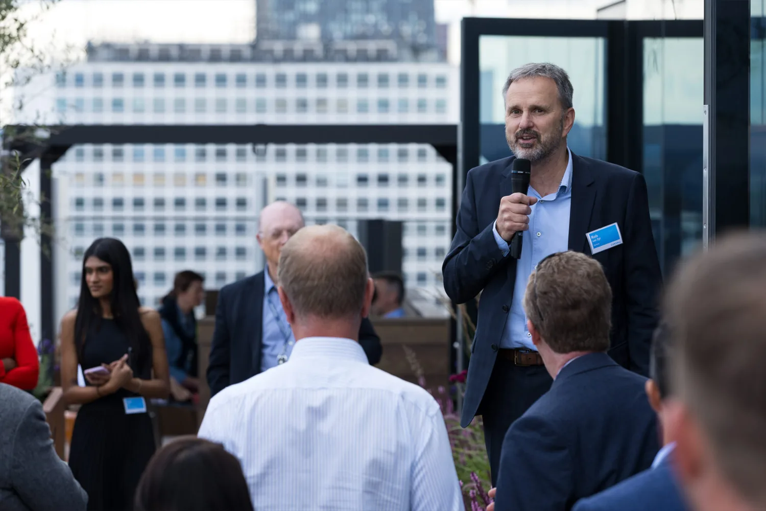 Presenter holding a microphone and speaking to the crowd on the outdoor terrace