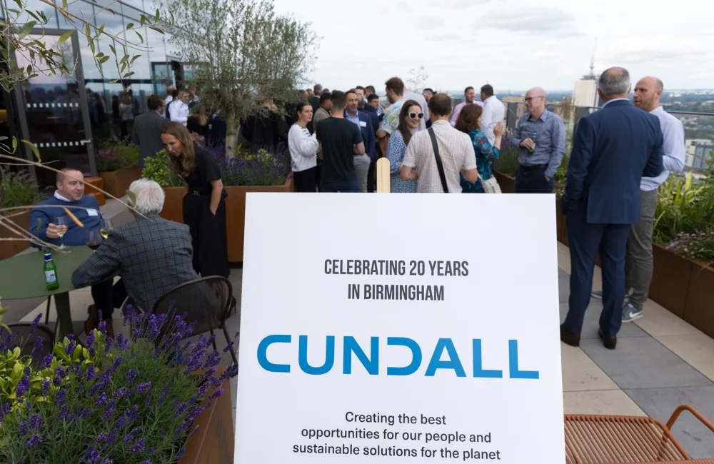 People socialising on an outdoor terrace with greenery and a board with Cundalls logo in the foreground