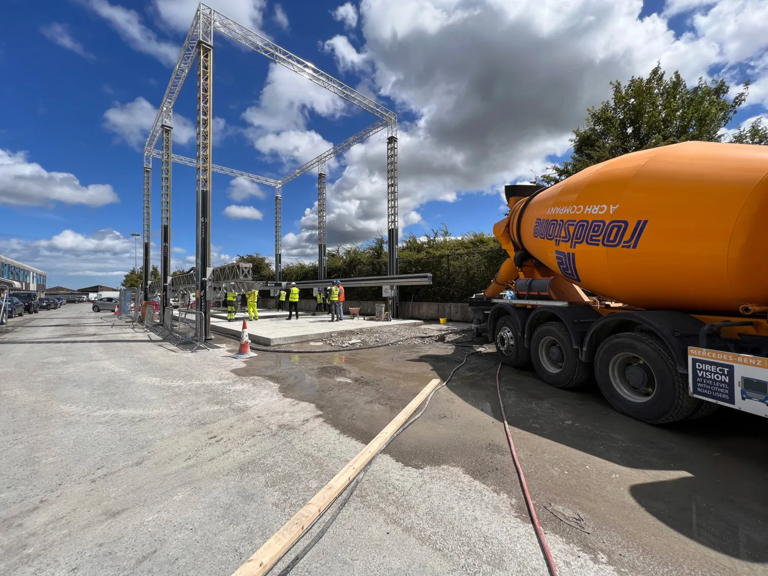 Building site with workers in high vis jackets and large, orange concrete mixer
