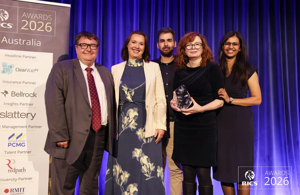 Five people posing on stage at the RICS Awards 2026 Australia event, with one person holding a glass award in front of a blue curtain backdrop.