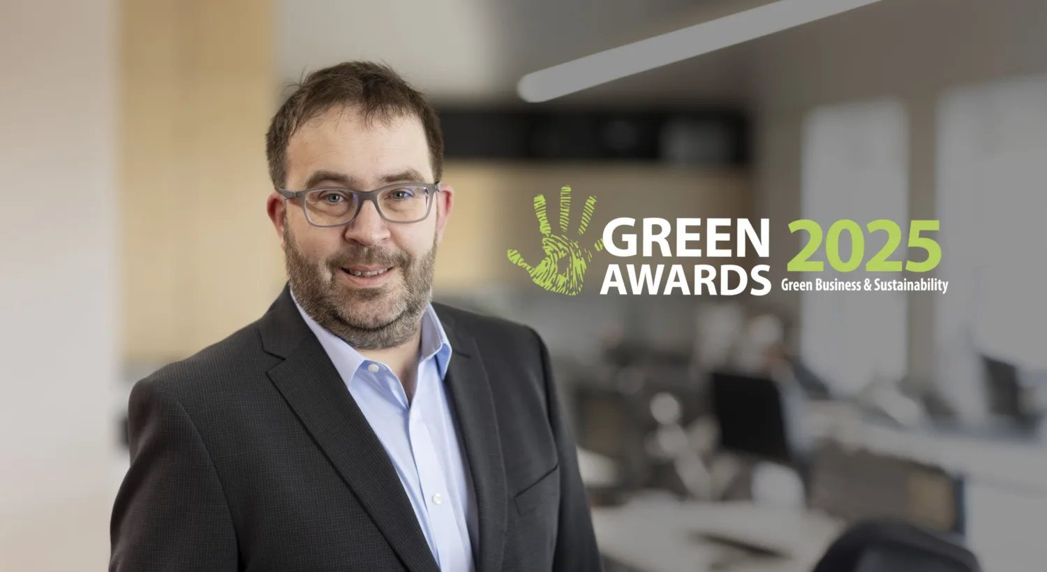 Photo of David Feighery in a blue shirt and black jacket standing in an office with text beside him saying Green Awards 2025