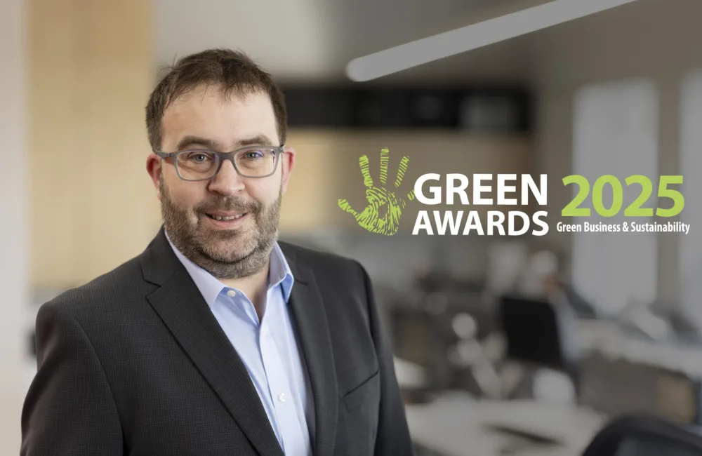 Photo of David Feighery in a blue shirt and black jacket standing in an office with text beside him saying Green Awards 2025