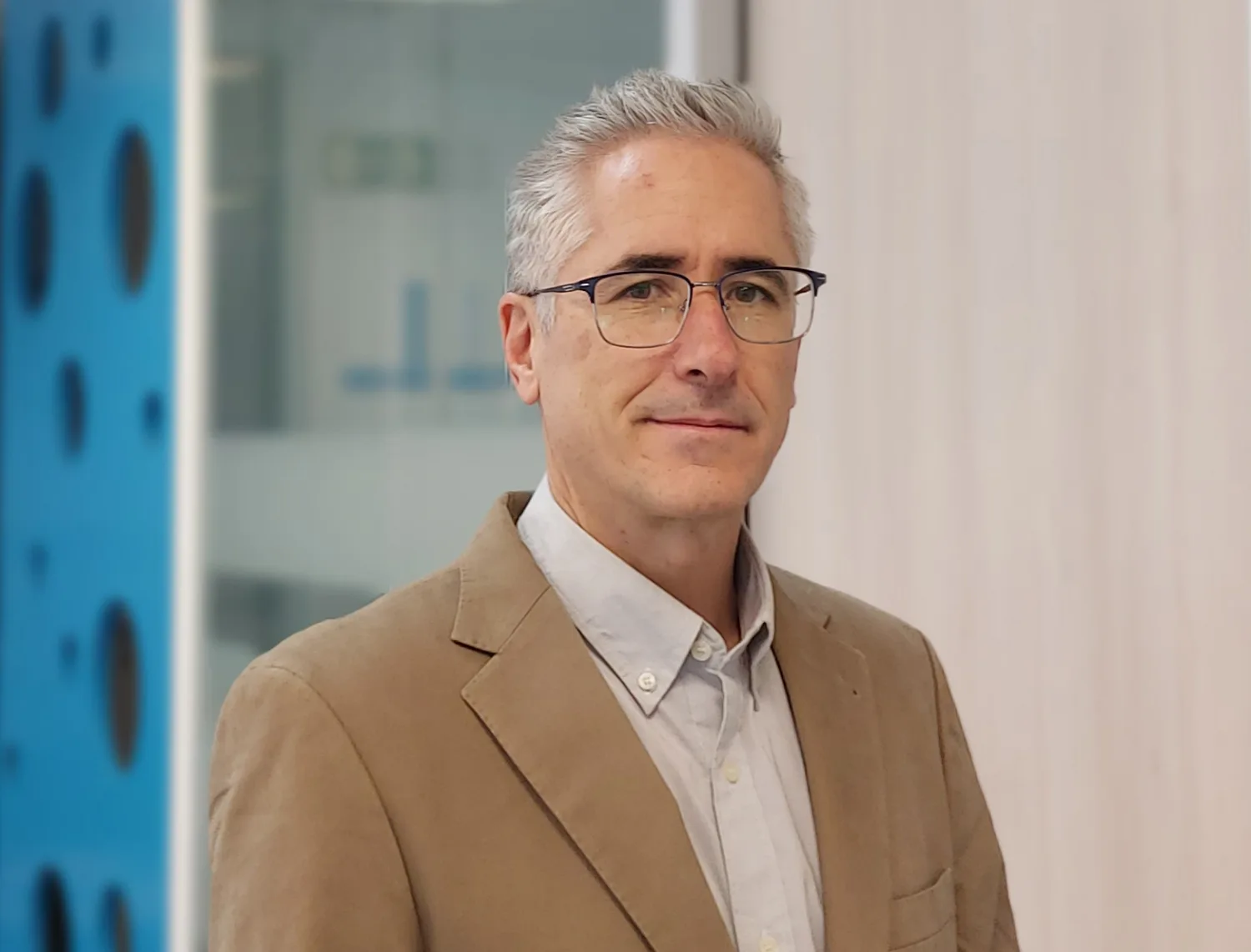 Cesar looking to camera in a beige jacket and pale open collar shirt in front of the meeting room door