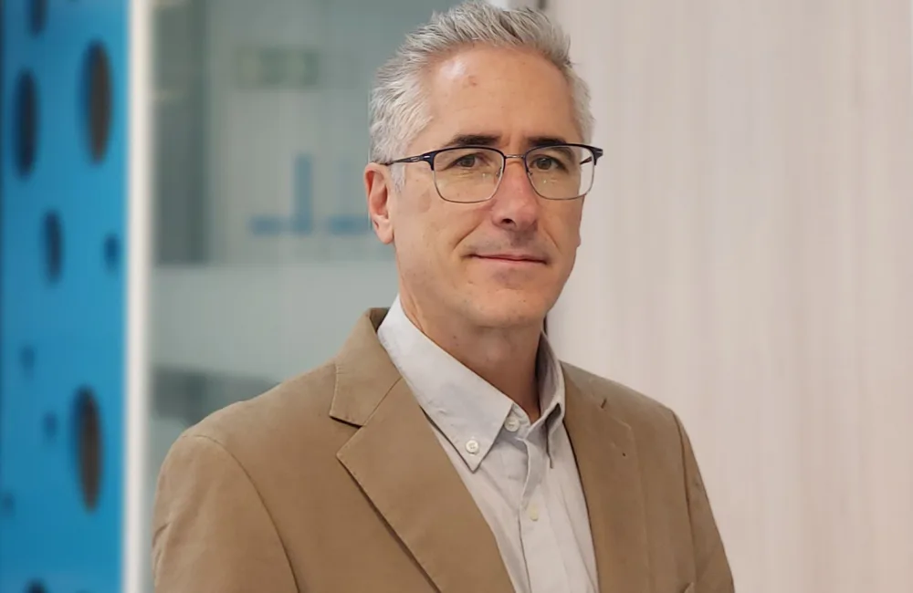 Cesar looking to camera in a beige jacket and pale open collar shirt in front of the meeting room door