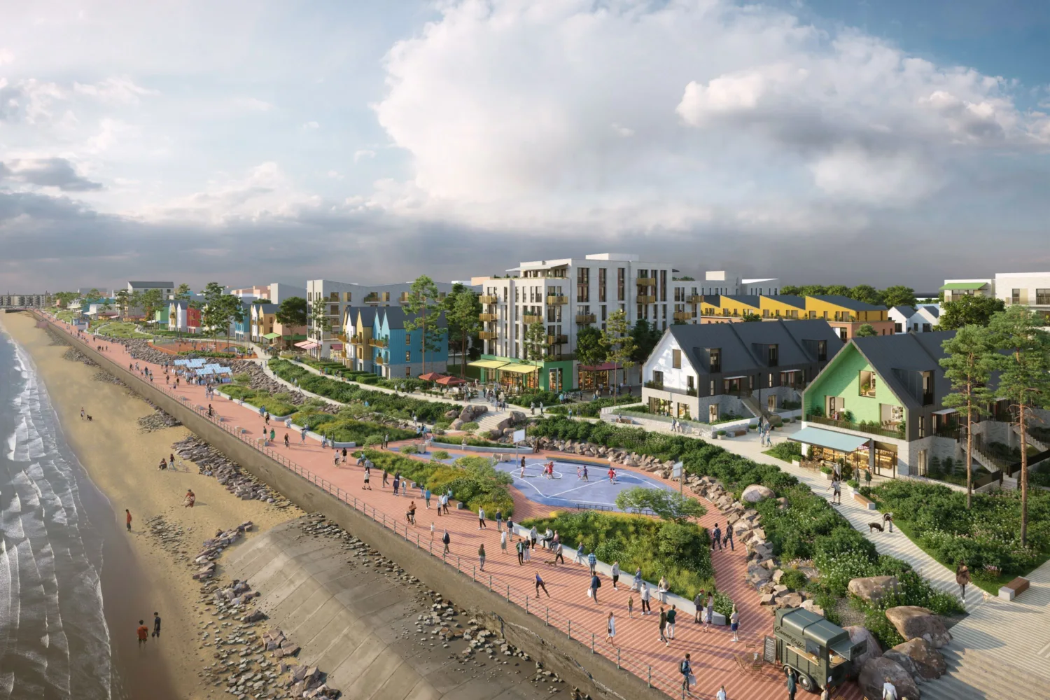 Coastal promenade with a sandy beach on the left and a pedestrian walkway with greenery, benches, and people on the right. Colourful houses and multi-story apartments are in the background under a partly cloudy sky.