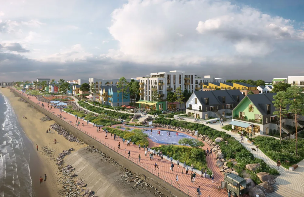 Coastal promenade with a sandy beach on the left and a pedestrian walkway with greenery, benches, and people on the right. Colourful houses and multi-story apartments are in the background under a partly cloudy sky.