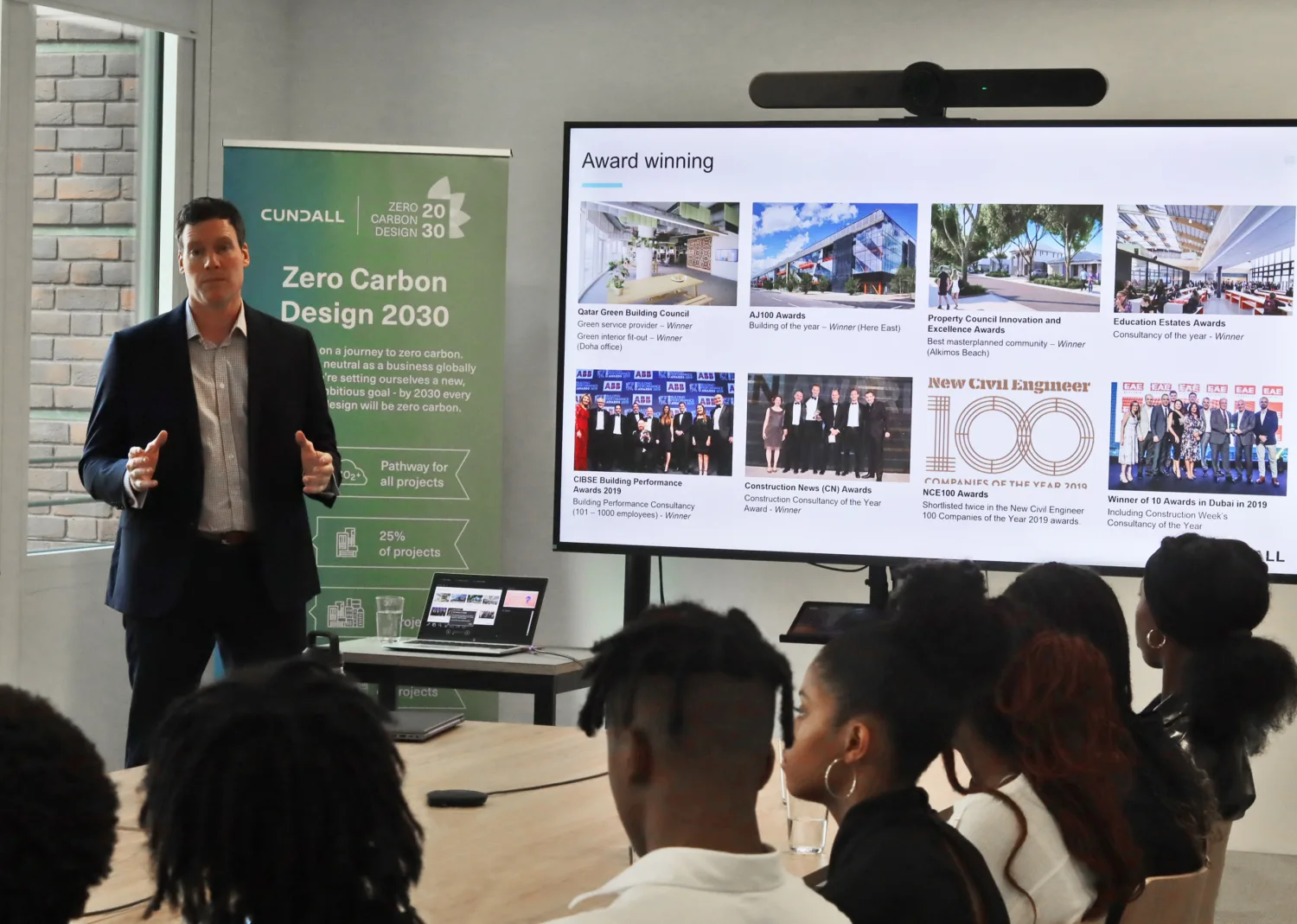 Rob stood in front of a roller banner next to a large screen presenting to the students
