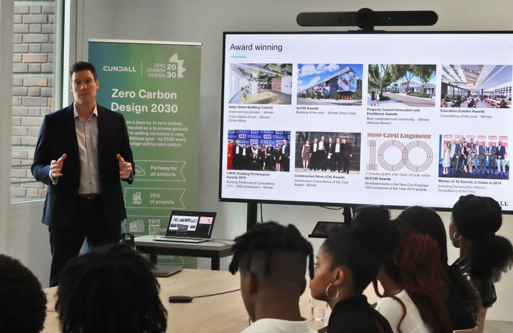 Rob stood in front of a roller banner next to a large screen presenting to the students