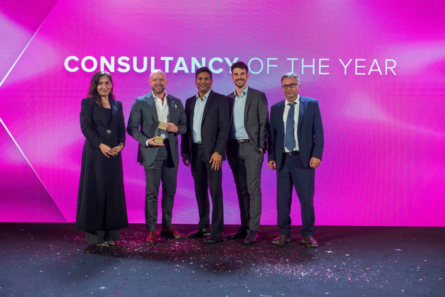 Five people standing on a stage with an award trophy in front of a screen displaying the text “CONSULTANCY OF THE YEAR”.