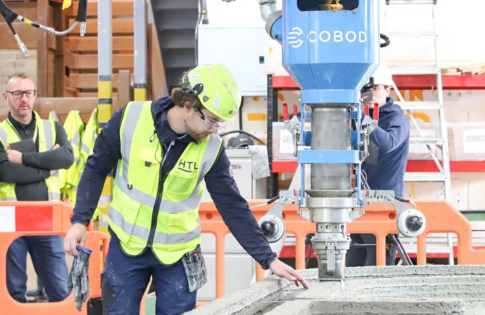 Workers in high vis jackets and hard hats overlooking a concrete printer on site