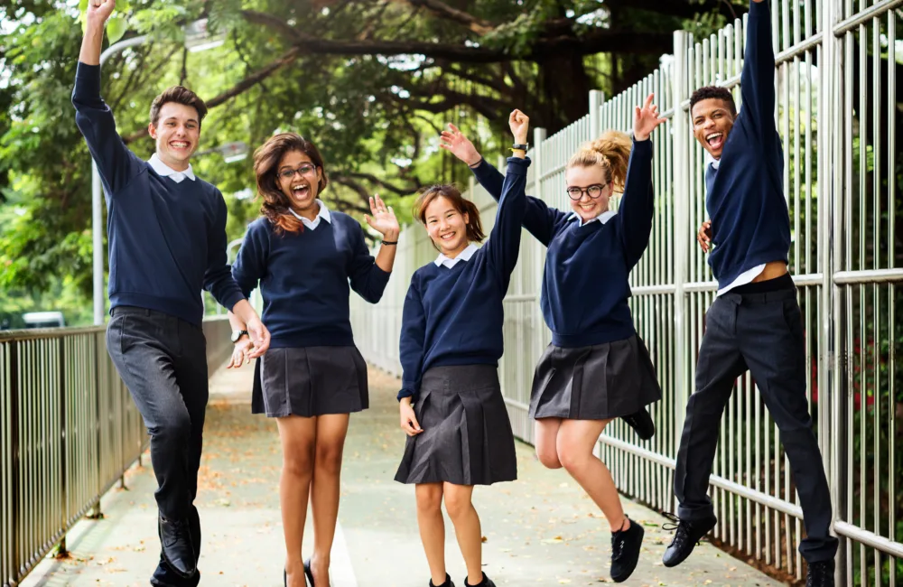 Students composed of male and female happily jumping on a walkway with trees in the background.