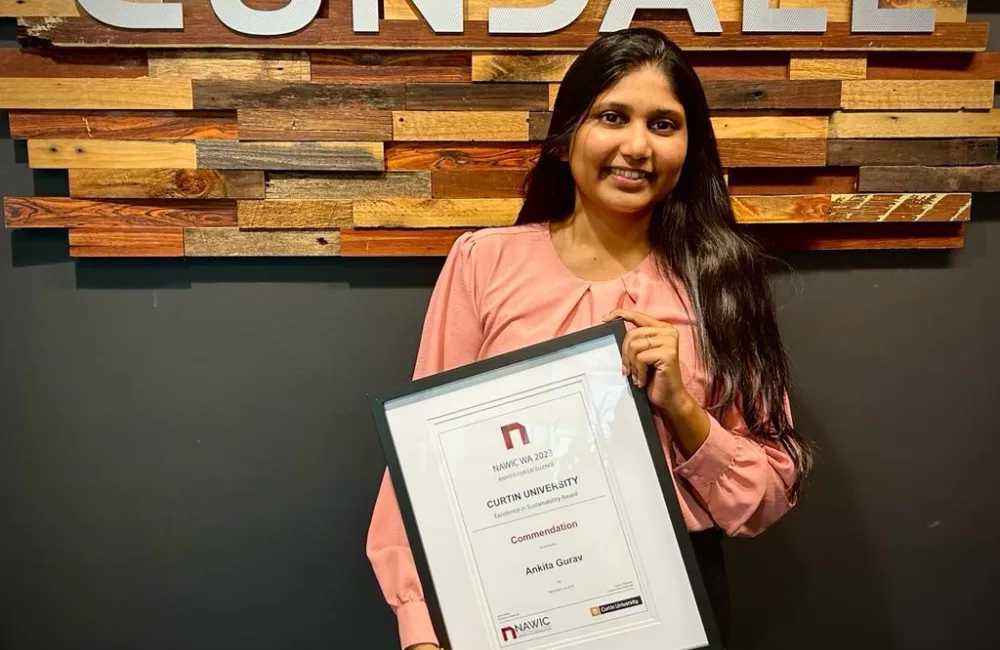 Ankita Gurav holding the award standing against a black wall with the Cundall logo in the background