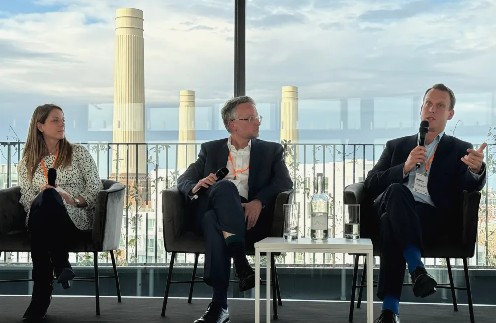 Three people sat down in a panel in front of a large window with Battersea Power Station in the background