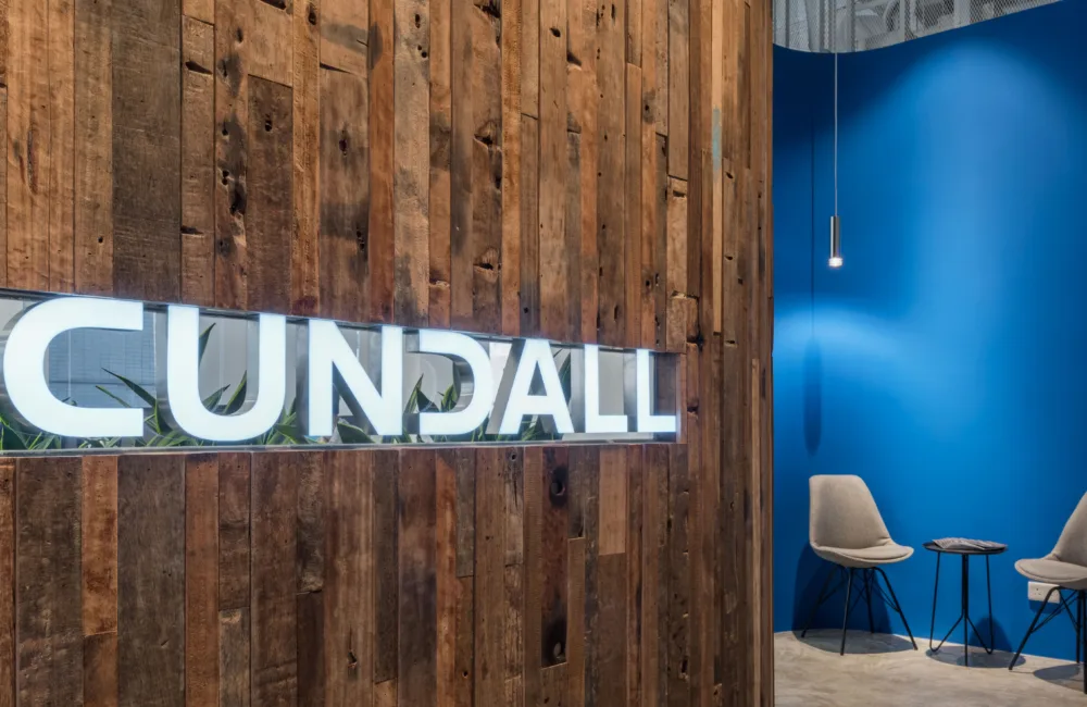 Wooden slat wall with lit Cundall logo with 2 chairs and small table against a blue wall