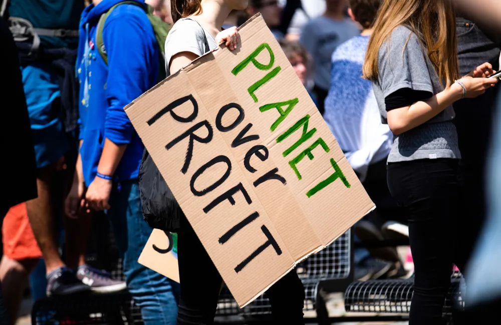 People at a protest carrying a carboard hand made sign that says 'Planet over profit'
