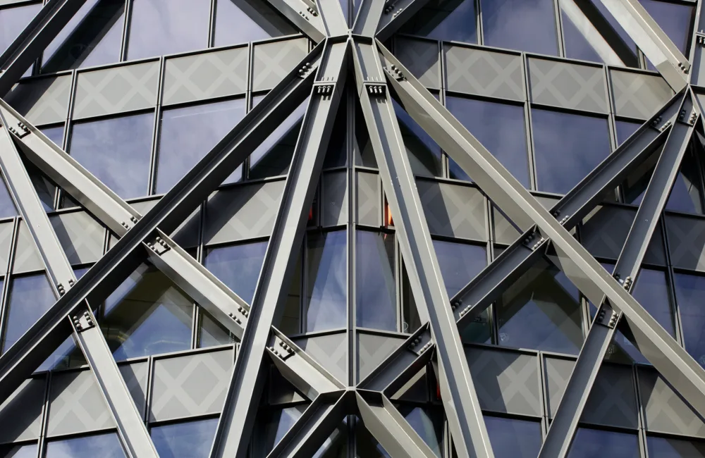 Close-up exterior of a windowed office building, with metallic beams arranged across the outside in a geometric pattern