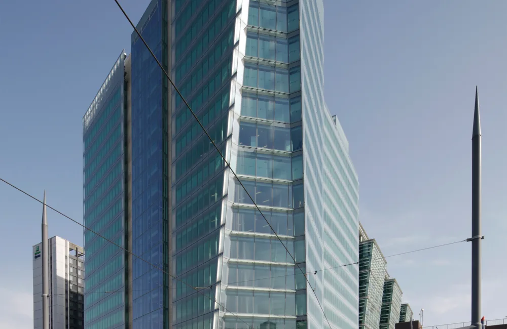 Exterior view of Three Snowhill, Birmingham, a tall windowed building against a blue sky, in the foreground is a blue tram at a tram stop