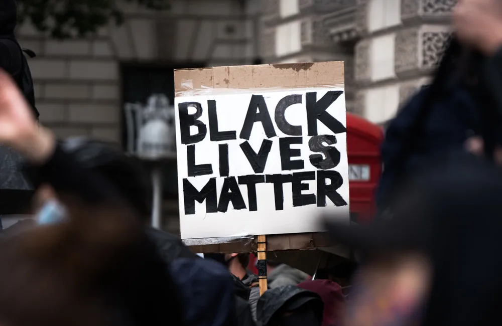 A group of unidentifiable people at a protest, one is holding a sign that reads in all capital letters 'Black Lives Matter'