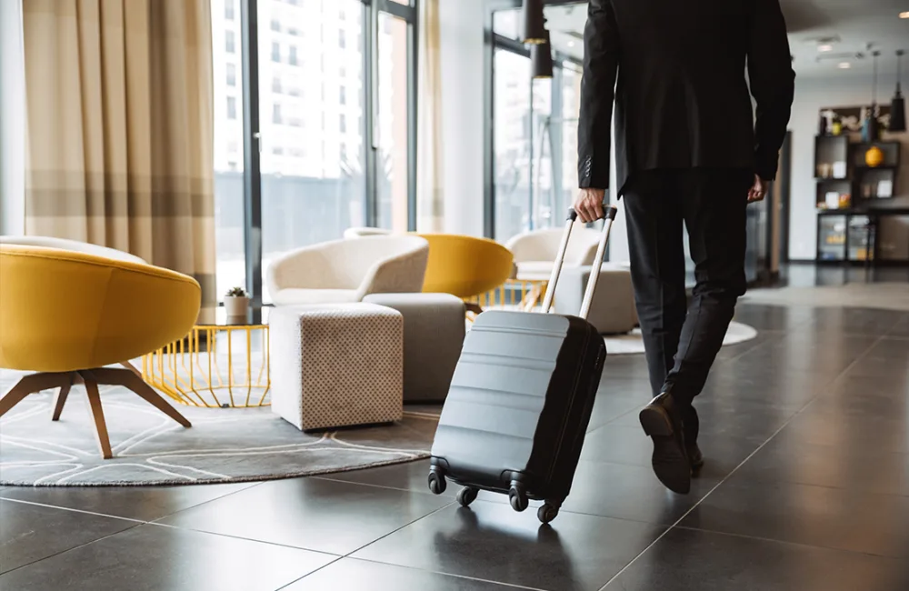Man in a black suit pulling a black four-wheeled suitcase in a clean hotel lobby