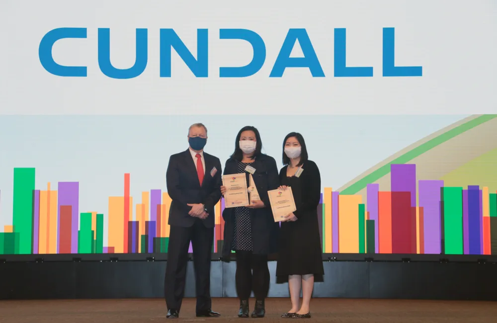 Cundall accepting the award on stage in front of a colourful backdrop and large Cundall logo