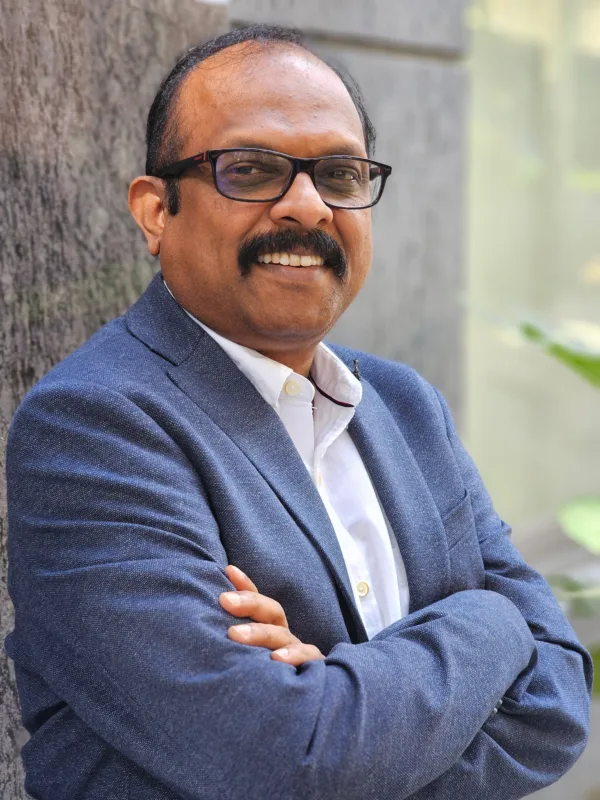 Rajeev smiling to camera with arms crossed outdoors