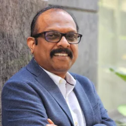 Rajeev smiling to camera with arms crossed outdoors