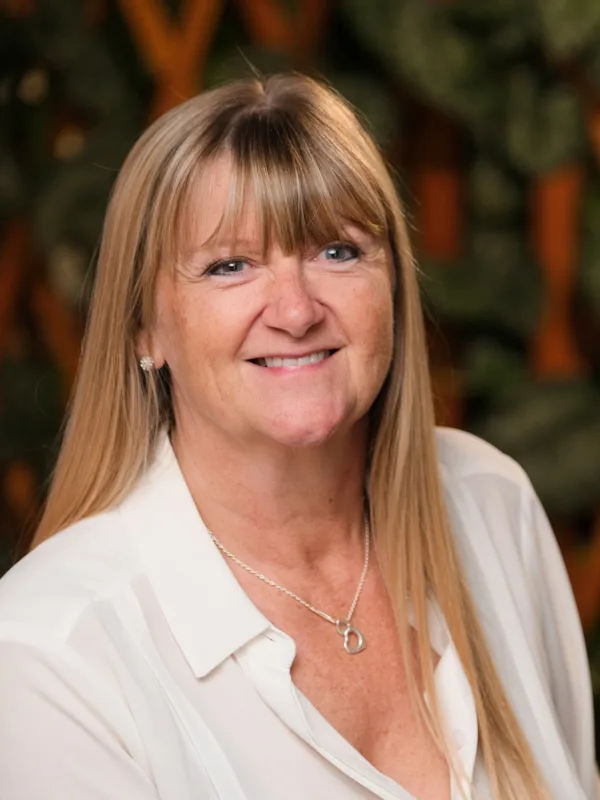 Belinda in a white blouse smiling to camera in front of a trelis wall