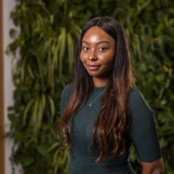Brittany Huggins in a dark green top in front of a green living wall