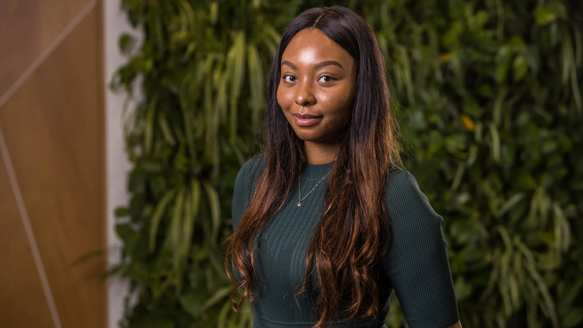 Brittany Huggins in a dark green top in front of a green living wall