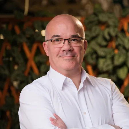 Danny Hillyard in a white shirt with glasses on and a plant terrace background