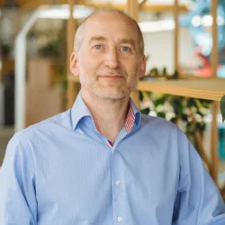 Tim Stidwill in blue shirt with wooden shelfing background with plants