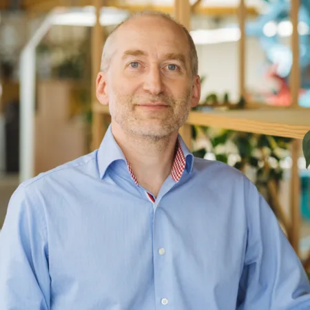 Tim Stidwill in blue shirt with wooden shelfing background with plants