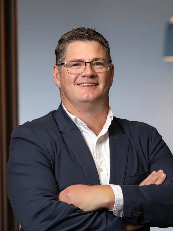 David Collins wearing a white shirt and navy blue suit jacket with his arms crossed