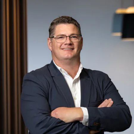 David Collins wearing a white shirt and navy blue suit jacket with his arms crossed