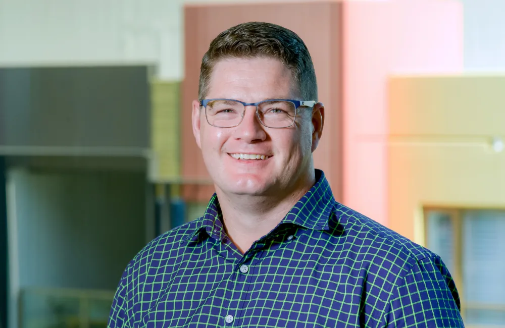 Dave in a dark blue checked shirt, outside smiling to camera