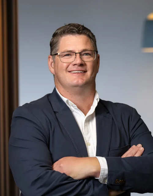 David Collins wearing a white shirt and navy blue suit jacket with his arms crossed