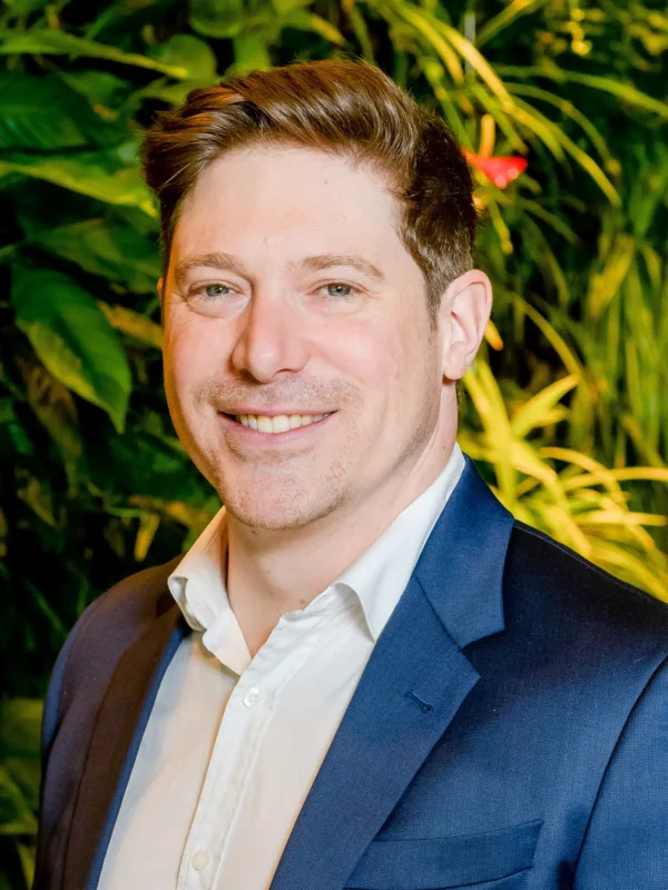 David in a blue suit jacket stood in front of a green plant wall