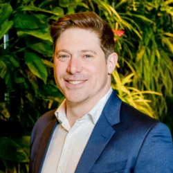 David in a blue suit jacket stood in front of a green plant wall