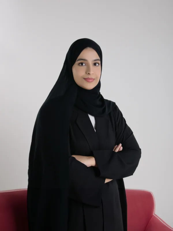 Athari Alqaydi posing for a photo with greyish studio background and a portion of a red sofa.
